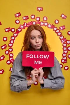 Beautiful redhead female holding FOLLOW ME sign, ask to be more active in Stock Photos