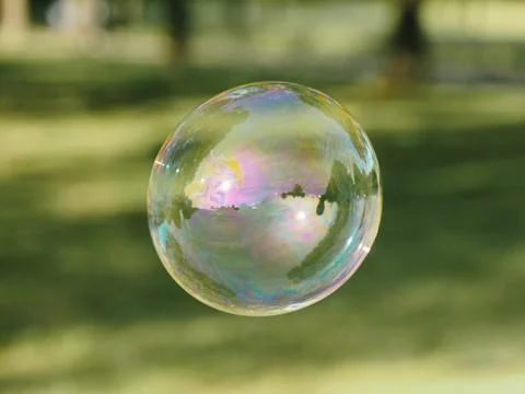 Beautiful round soap bubble floating above green grass in the countryside. Stock Photos