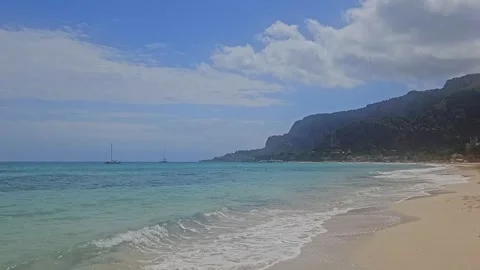 A beautiful sandy beach borders crystal-clear turquoise water with sailboats Stock Footage 337958947