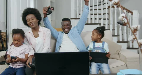 Beautiful satisfied smiling young black-skinned family with kids sitting on soft Stock Footage 144343785