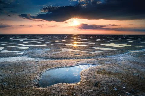 Beautiful scenery of the sunset reflected in a mudflat under the cloudy sky Stock Photos