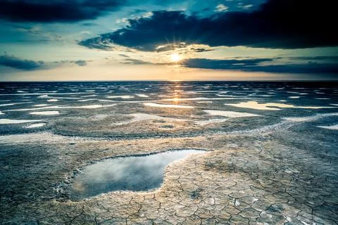 Beautiful scenery of the sunset reflected in a mudflat under the cloudy sky Stock Photos