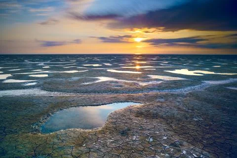 Beautiful scenery of the sunset reflected in a mudflat under the cloudy sky Stock Photos