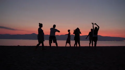 Beautiful sea sunset background, crowd of happy cheerful friends dancing Vidéo 135800702