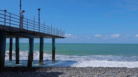 Beautiful sea waves with foam at the pebble beach and the old pier Stock Footage