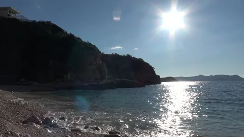 Beautiful seascape featuring bright sun with dark rocky cliffs under blue sk Stock Footage 332860938