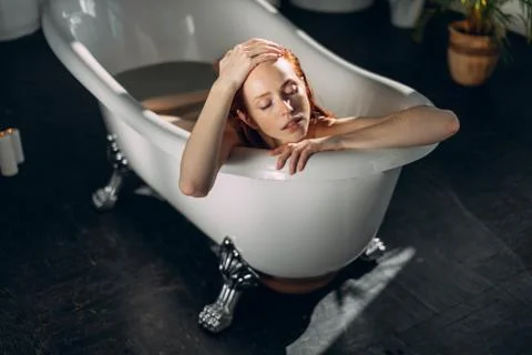 Beautiful seductive young red-haired lady with bare shoulders in bathtub. Stock Photos