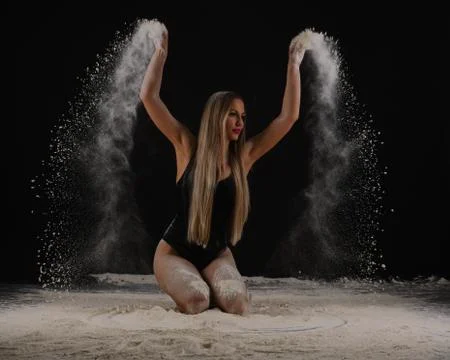 Beautiful sensual slim dancer throwing dust, flour, powder on black background. Stock Photos