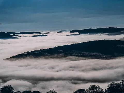 Beautiful shining sun over clouds covering mountains Stock Photos