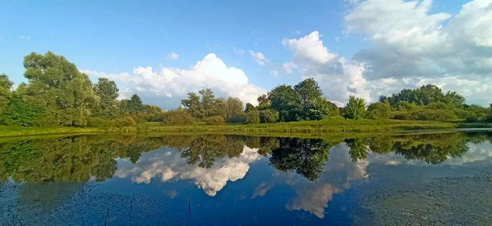 Beautiful sky and clouds reflection in the calm water of a scenic forest lake Stock Photos