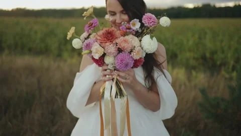 A beautiful smiling bride stands by the field and brings a delicate bouquet of Vídeo Stock 169074489