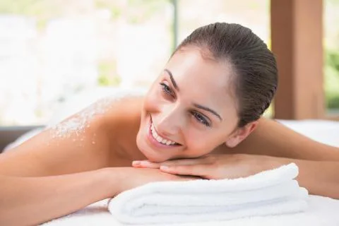 Beautiful smiling brunette lying on massage table with salt scrub on back Stock Photos