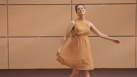 Beautiful smiling brunette model posing near yellow wall in dress Stock Footage 141810724
