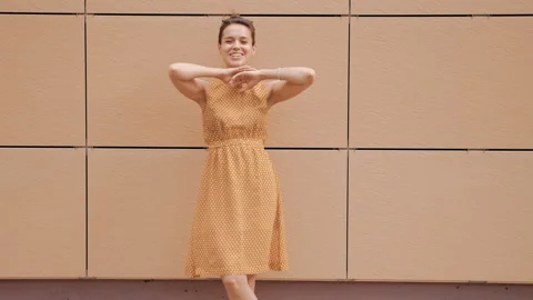 Beautiful smiling brunette model posing near yellow wall in hipster dress Stock Footage 141811033