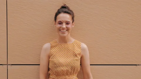 Beautiful smiling brunette model posing near yellow wall in hipster dress Stock Footage 141811090