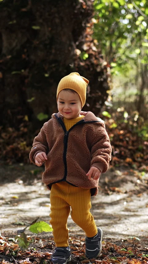 Beautiful smiling kid wearing cap and jacket walking in nature. Baby boy steps Vídeos de archivo 328627705