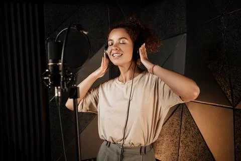 Beautiful smiling singer girl in headphones dreamily recording song in Stock Photos