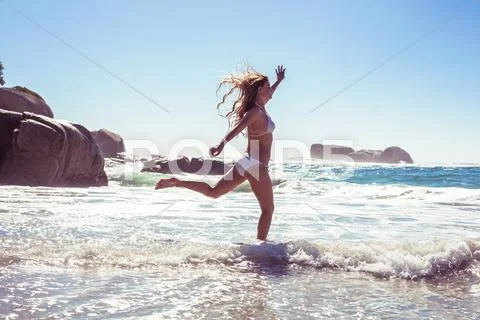 Beautiful smiling woman in white bikini skipping on the beach Stock Photos