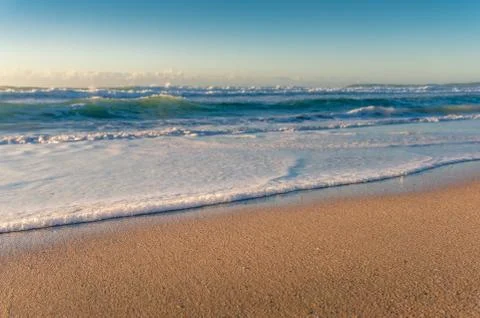 Beautiful soft waves with white foam crashing at yellow sandy shore Stock Photos