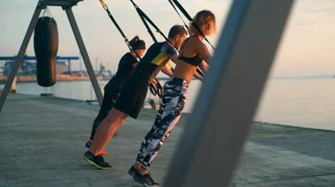 Beautiful sportive people training arms with trx at sea sunrise. Slow motion. Stock Footage 67987553