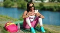 Beautiful sportswoman sits near lake and uses cell phone HD Footage