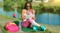 Beautiful sportswoman sits near lake and talks via tablet computer HD Footage