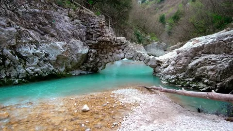 Beautiful stone semi-arch bridge over a river with blue water in the mountains Stock Footage 270062405