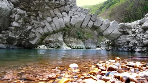 Beautiful stone semi-arch bridge over a river with blue water in the mountains Stock Footage 270062430