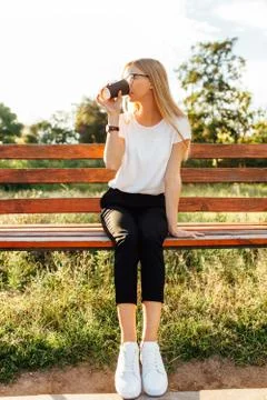Beautiful student with glasses drinking coffee, sitting on a bench in the Par Stock Photos