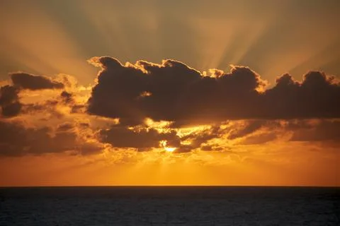 The beautiful sun behind clouds rises brilliantly over the Atlantic Ocean i.. Stock Photos
