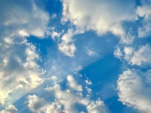 Beautiful Sun Rays Breaking Through Fluffy White Clouds in a Vibrant Blue Sky Stock Photos