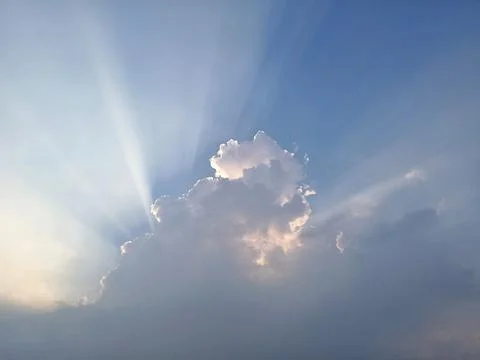 Beautiful sun rays shining from behind a cloud in the blue sky. Фото