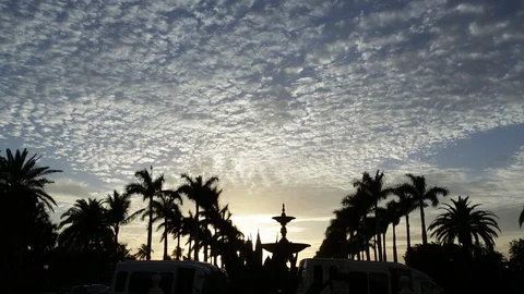 A Beautiful sunset and cloud formations silhouette a fountain and palm trees Stock Footage 89240805