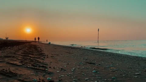 Beautiful sunset beach with gentle waves and people walking by the sea Stock Footage 333834191