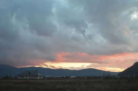 Beautiful sunset behind mountains with dramatic clouds and distant buildings in Stock Photos