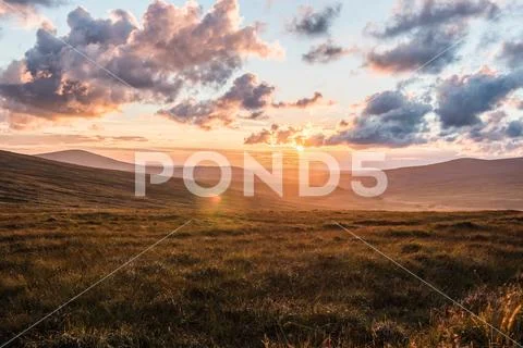 Beautiful sunset with cloudy sky and lens flare on a grass hill in Ireland Stock Photos