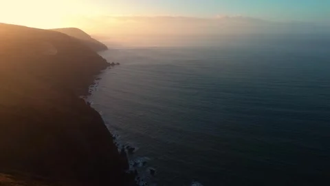 Beautiful Sunset Coastline with Hazy Setting Sun Across Blue Ocean and Crashing Stock Footage 301324127