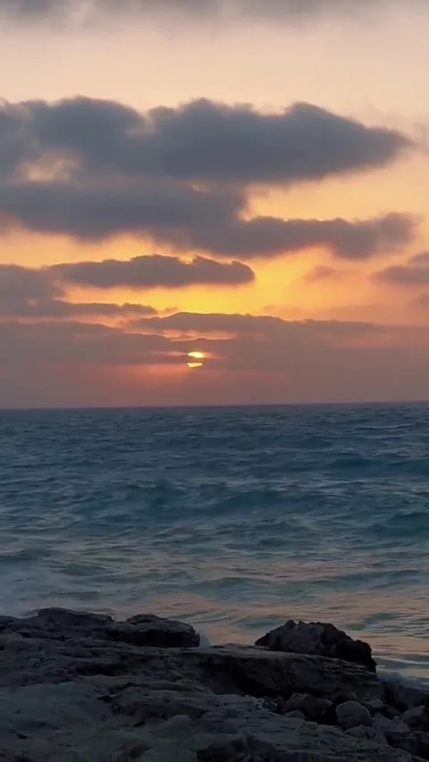 A beautiful sunset over the ocean with dark clouds and rocky foreground Vídeos de archivo 334163786