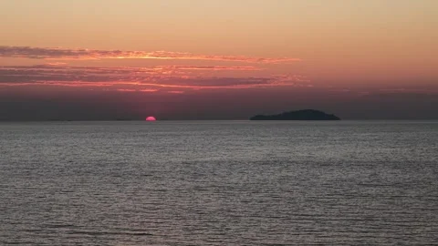 Beautiful sunset over the ocean with a small island in the distance Видео 332229236