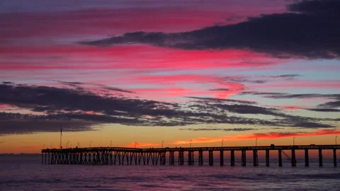 Beautiful sunset with pink clouds over a long pier stretching into ocean wate Stock Footage 337778050