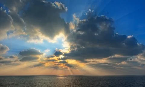 Beautiful sunset with rays of light. Gray clouds and calm sea or ocean. Stock Photos