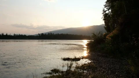 Beautiful sunset, rays of the sun in river. River flows. Trees, grass, mountains Stock Footage 121273551