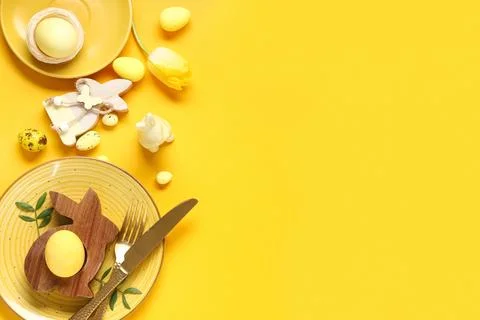 Beautiful table setting with Easter eggs, toy bunnies and tulip flower on yel Stock Photos