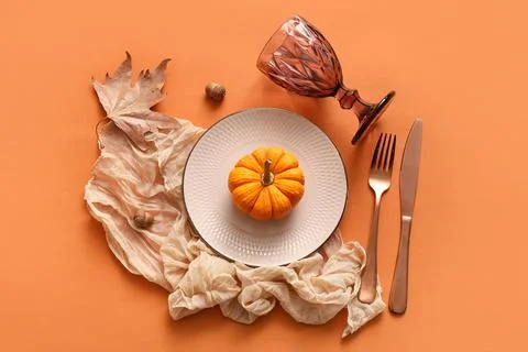 Beautiful table setting with pumpkin, acorns and autumn leaf on orange backgr Stock Photos