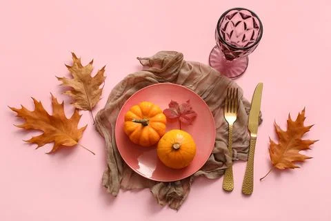 Beautiful table setting with pumpkins and autumn leaves on pink background Stock Photos