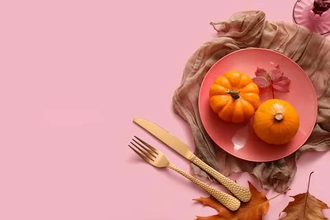 Beautiful table setting with pumpkins and autumn leaves on pink background Stock Photos