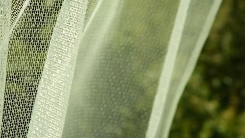 Beautiful thin curtain moves in the wind against the backdrop of a green gard Stockbeeldmateriaal 105462680