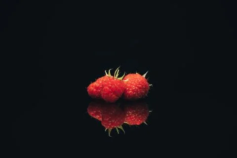 Beautiful three fresh raspberry on a black glass table dark background. Foto stock