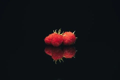 Beautiful three fresh raspberry on a black glass table dark background. Foto stock