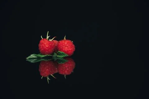 Beautiful three fresh raspberry on a black glass table dark background. Stock Photos